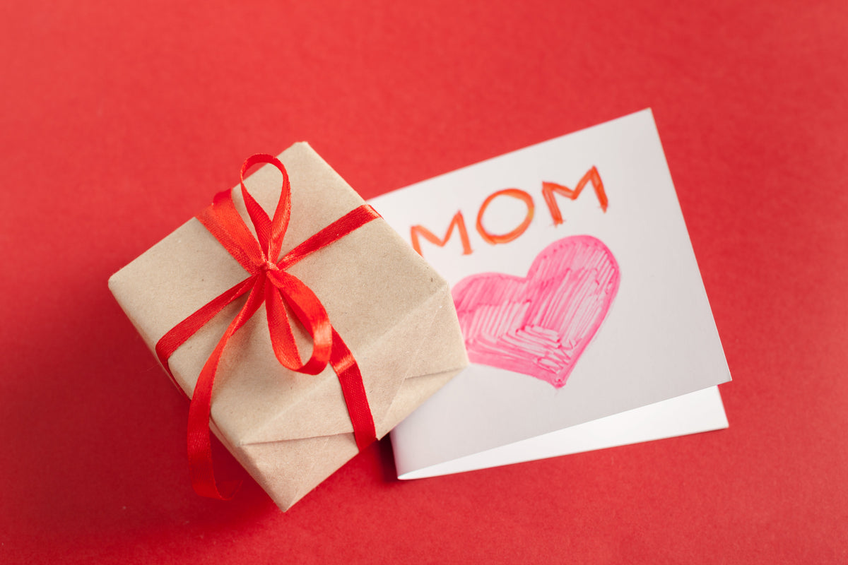 Mother’s Day gift box with red ribbon next to a “MOM” card on a red background