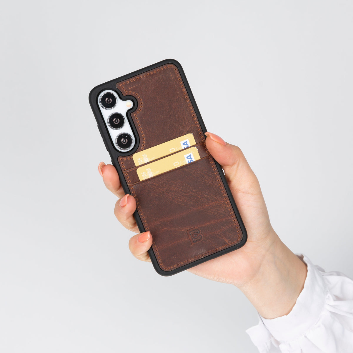 A hand holding a brown Samsung Galaxy S25 Plus phone case with a leather exterior and dual card slots visible.