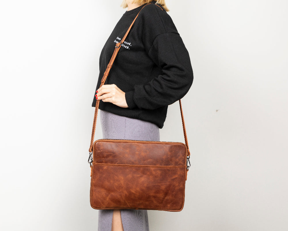 Person holding a brown leather bag against a plain background