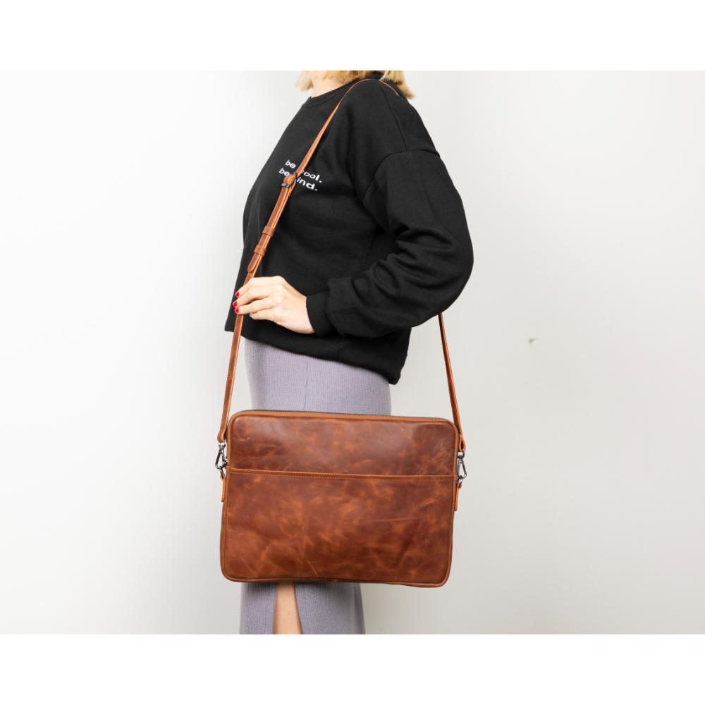 Person wearing a black sweatshirt with a brown leather bag over their shoulder on a white background