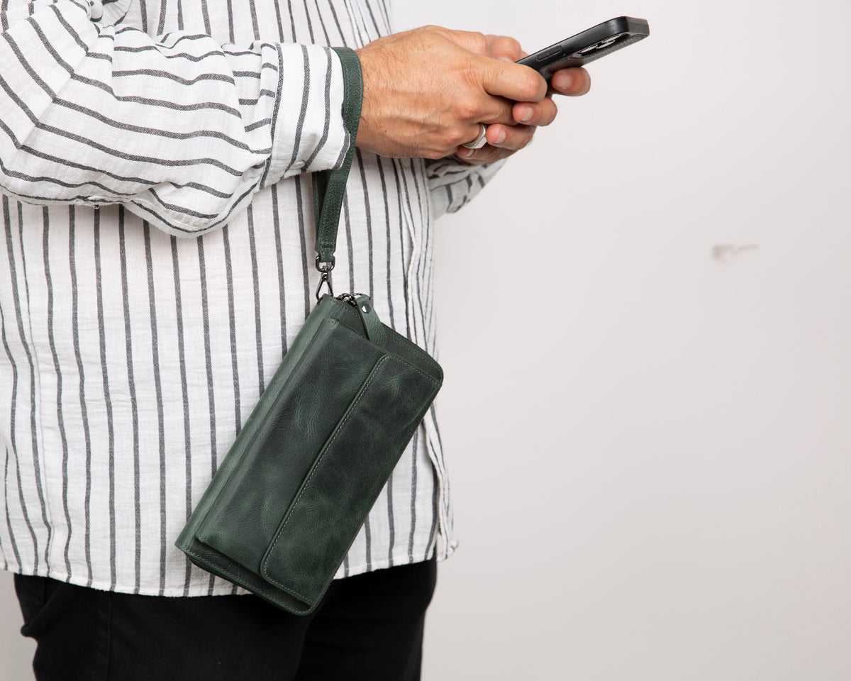 Person holding a green leather clutch bag and a smartphone against a plain background