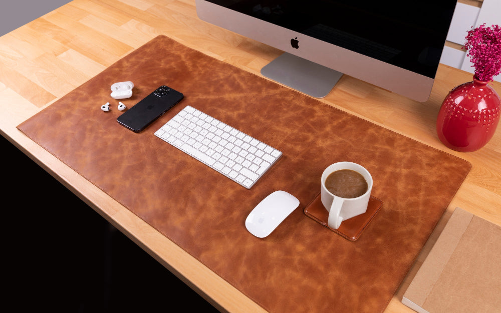 Desk setup with a computer, keyboard, mouse, and coffee cup on a large brown leather desk pad.