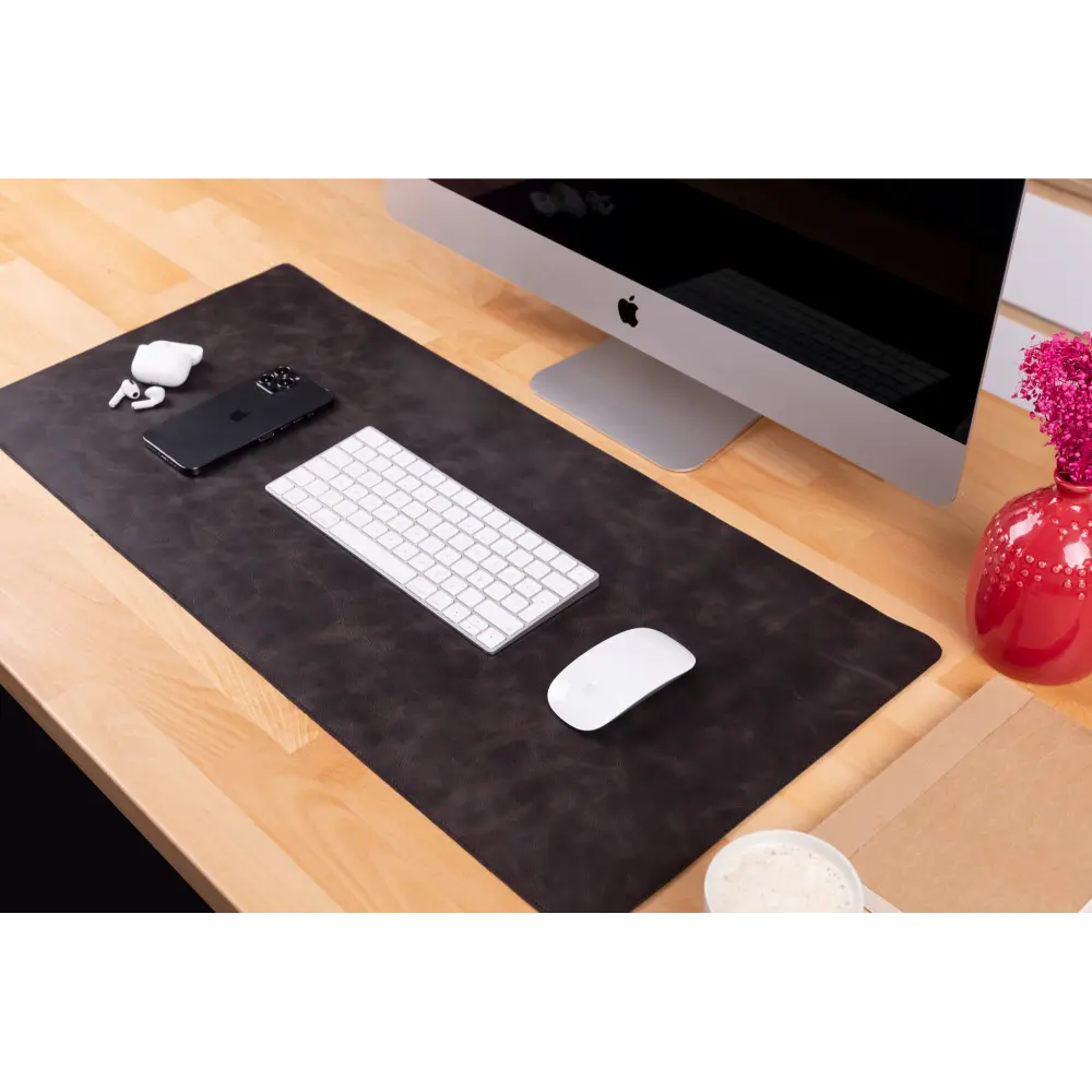 Black desk mat with computer, keyboard, mouse, and other items on a wooden desk.