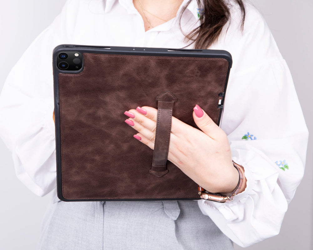 Person holding a brown leather tablet case with a white shirt and light gray pants.