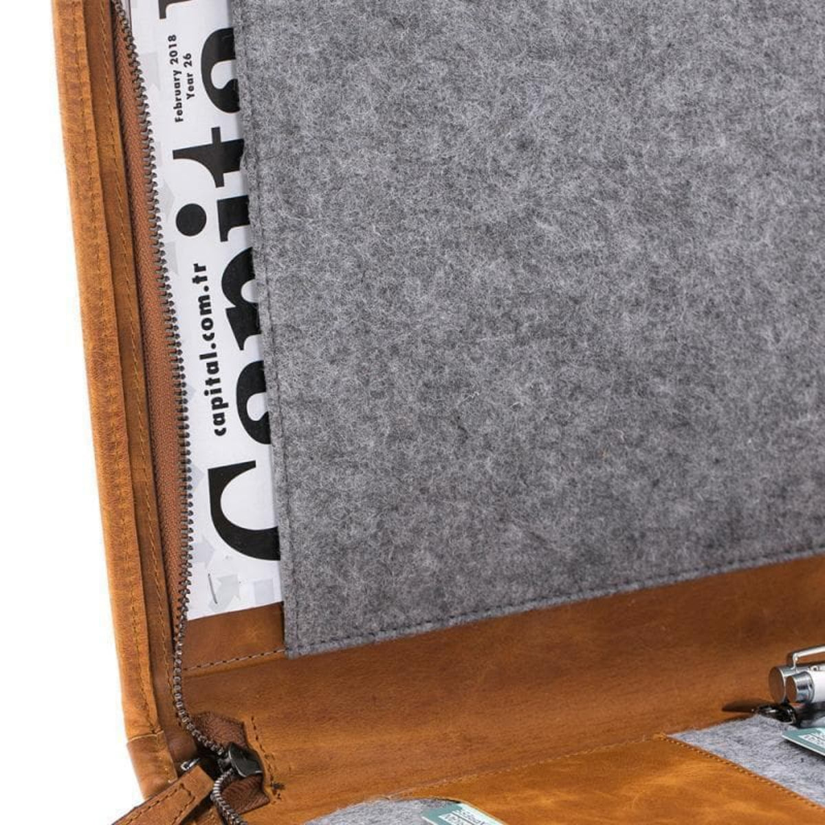 Close-up of a brown leather case with a gray felt interior, featuring a magazine inside.