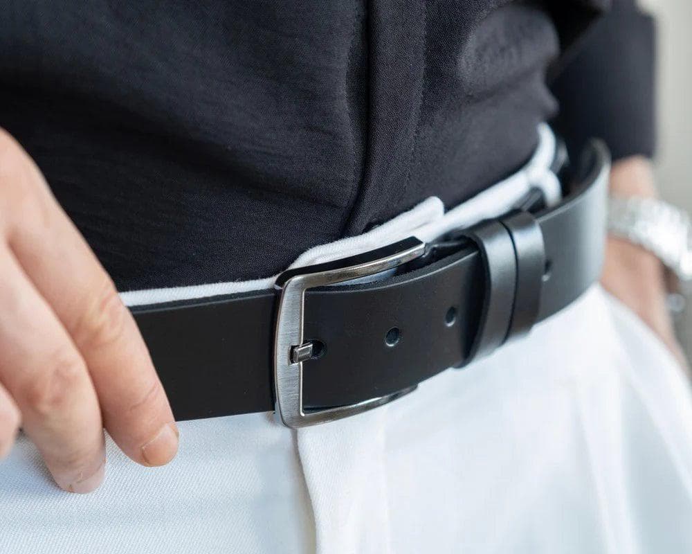 Person adjusting a black belt with a silver buckle on a plain background
