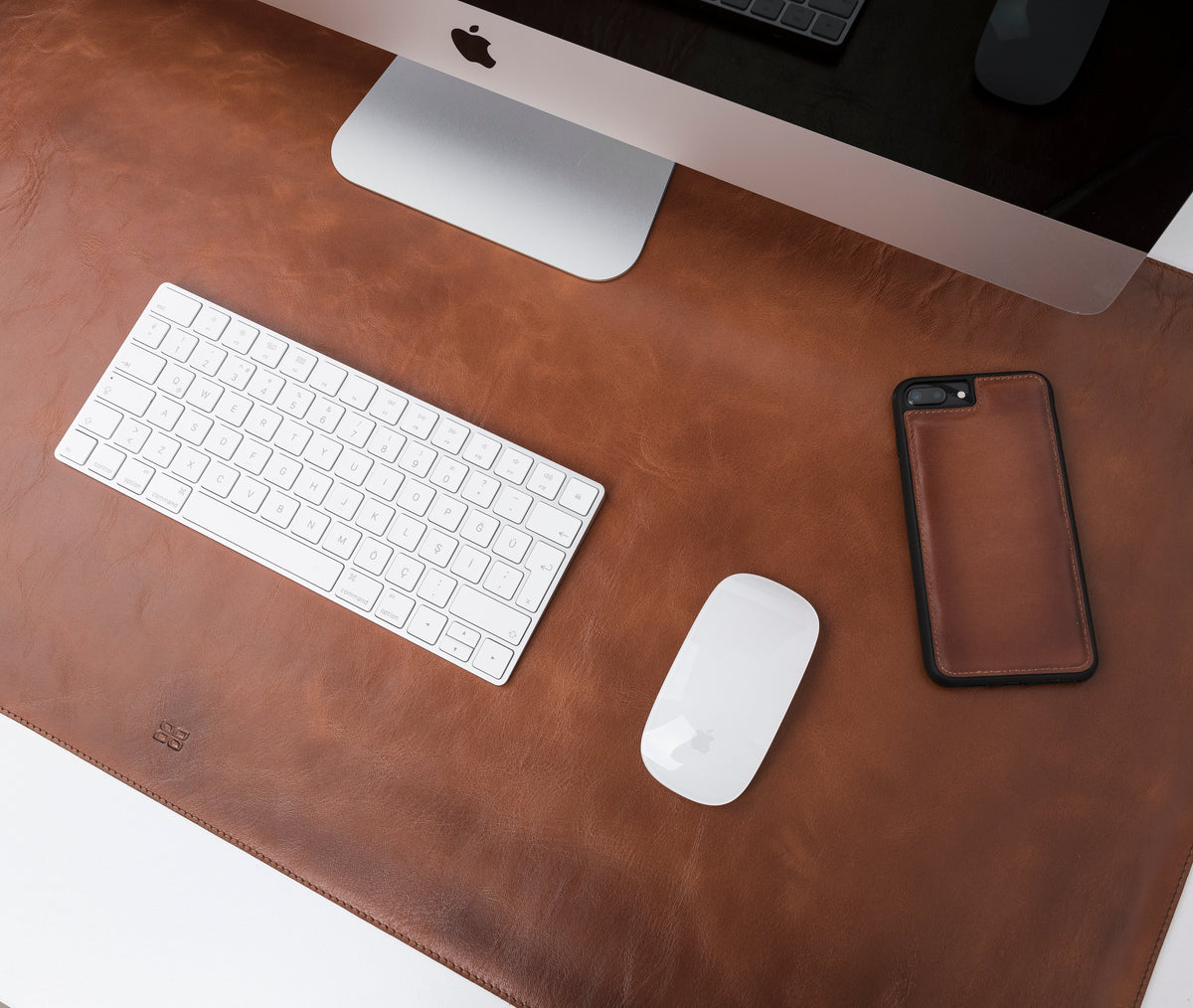 A black genuine leather desk mat displayed on a desk with a computer monitor, keyboard, mouse, and a mobile phone.