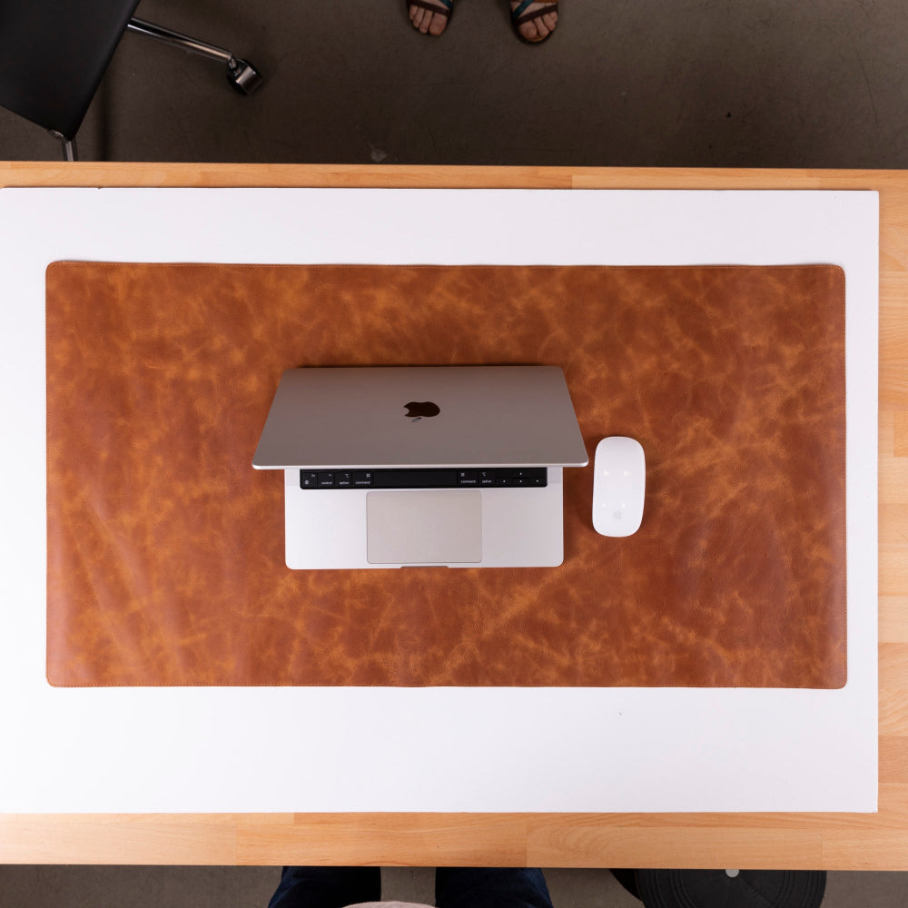 Laptop on a brown leather desk pad with a white mouse