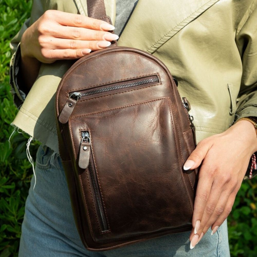 Brown leather crossbody bag held by a person outdoors