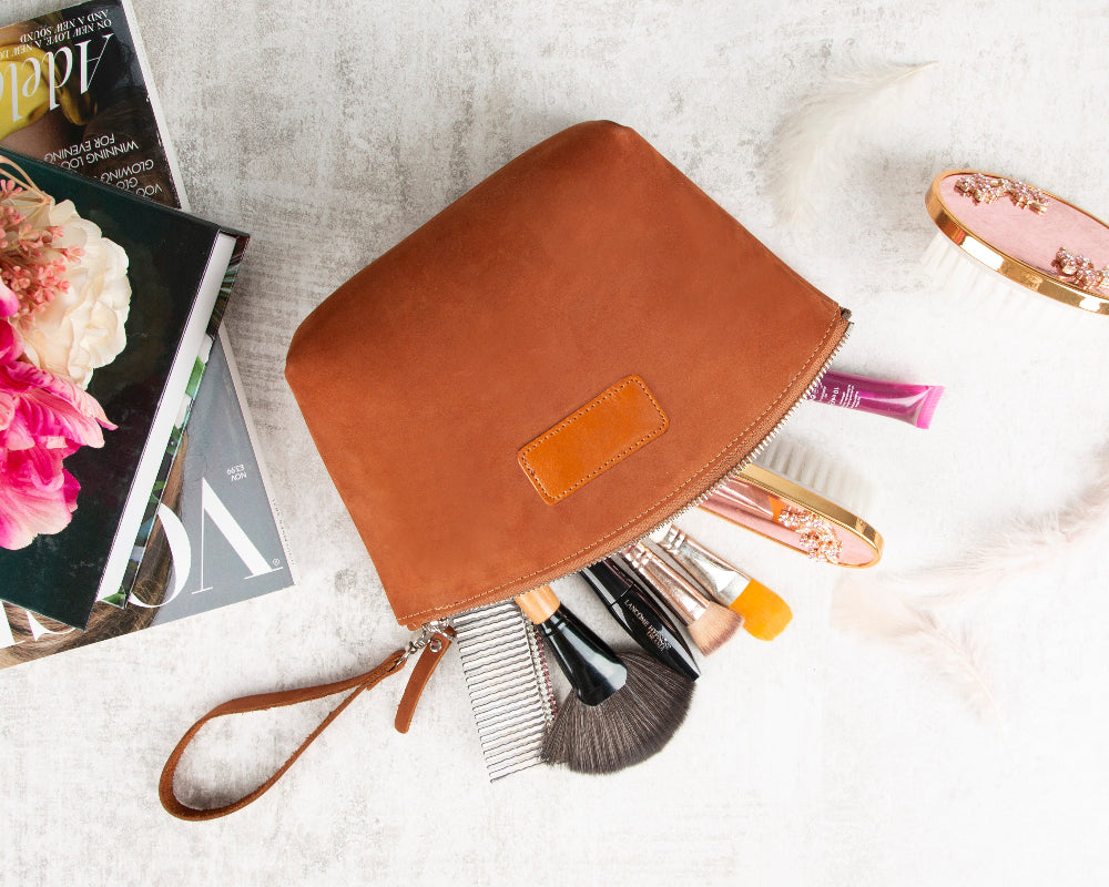 Brown makeup pouch with cosmetic tools on a textured surface