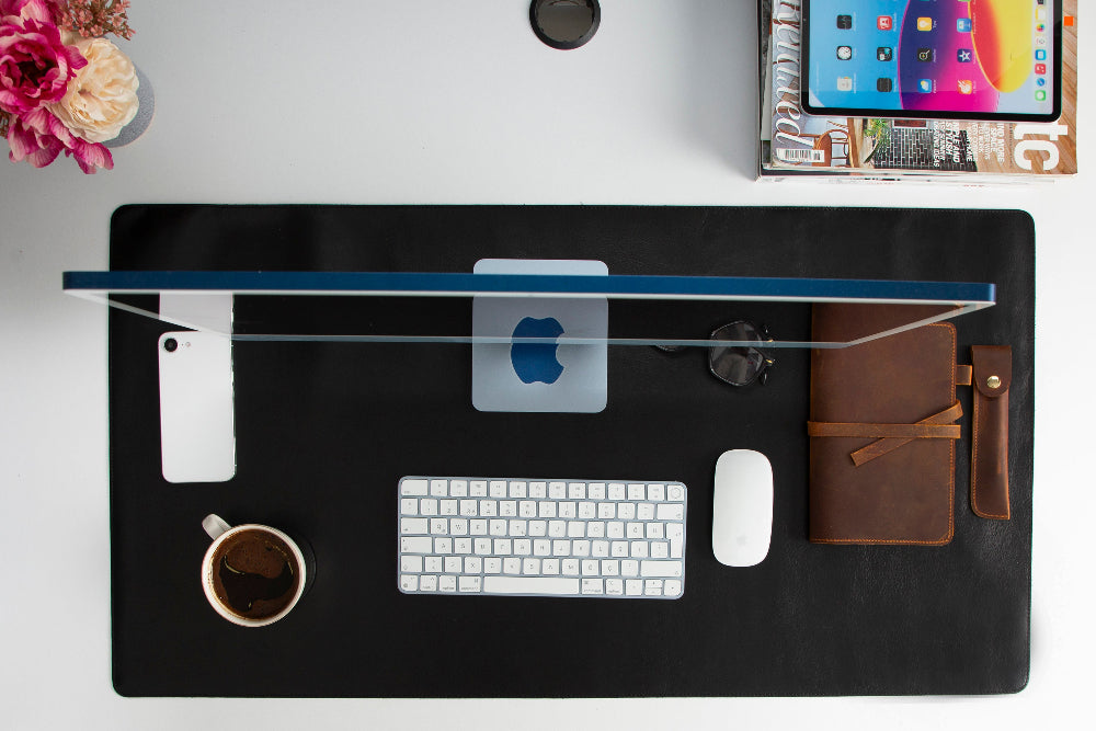 Black desk mat with office items including a laptop, keyboard, mouse, and phone on a white surface.