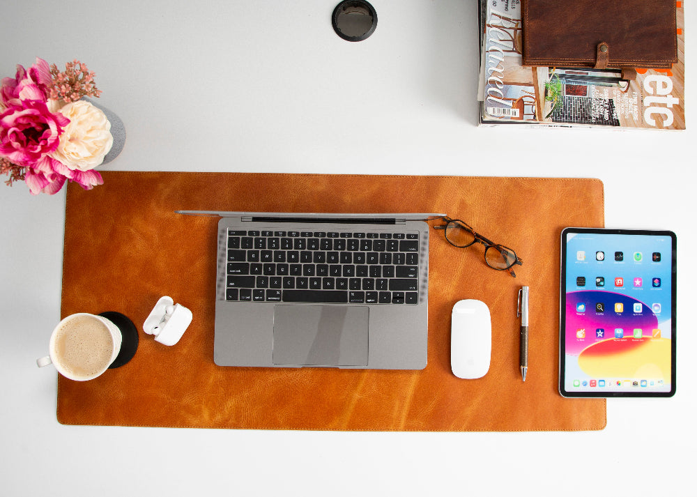 Desk setup with laptop, tablet, coffee cup, and flowers on a wooden desk.