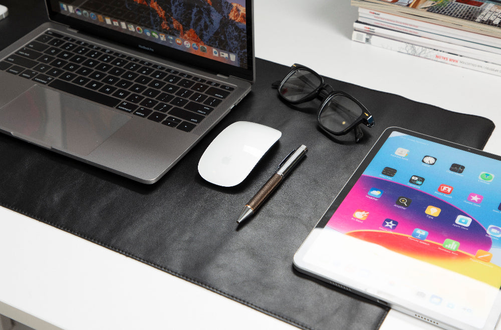 Laptop, tablet, mouse, and pen on a desk with a black leather pad