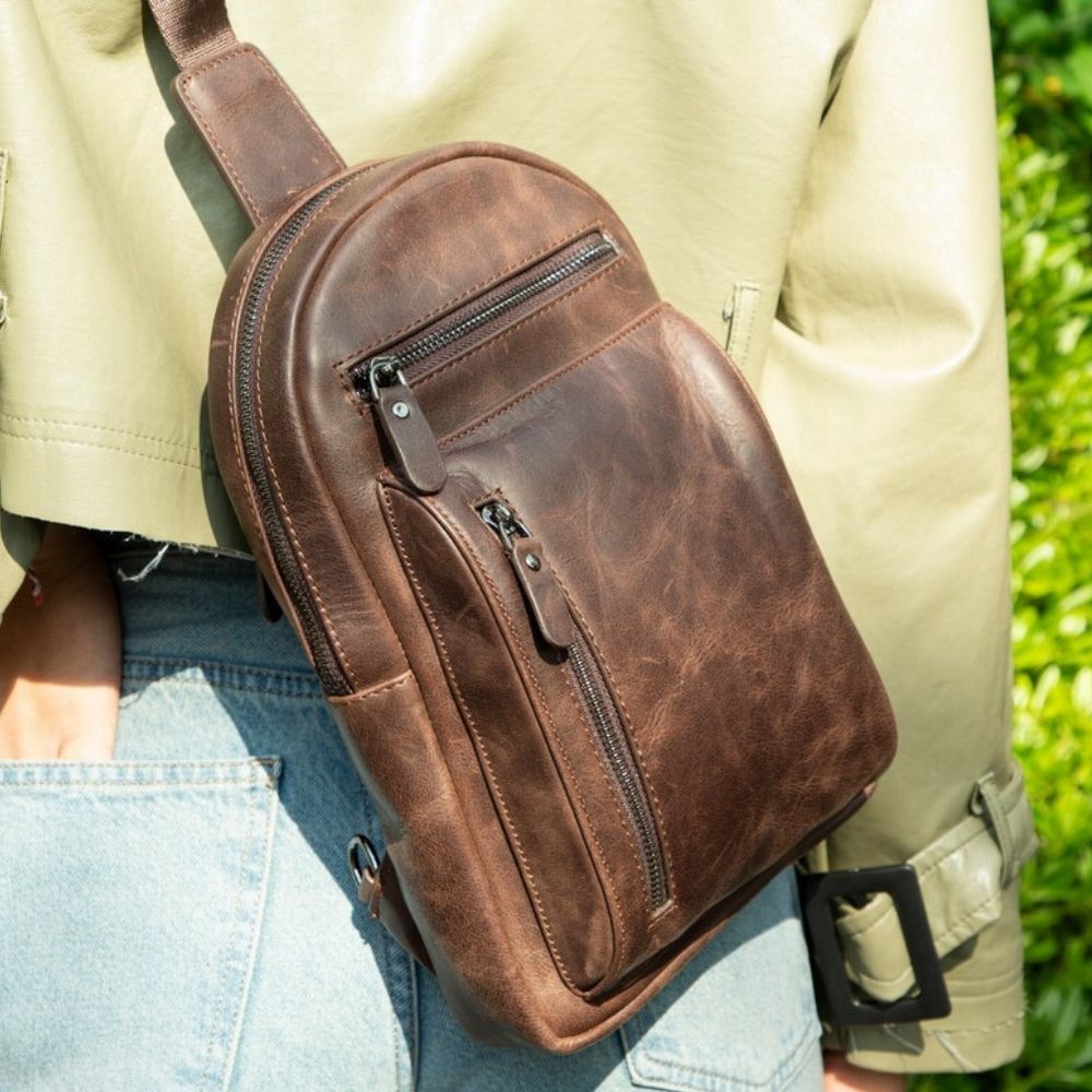 Brown leather crossbody bag worn by a person outdoors
