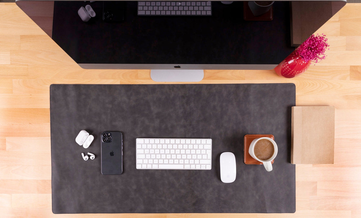 Desk setup with a large mouse pad, keyboard, phone, earbuds, and coffee cup.