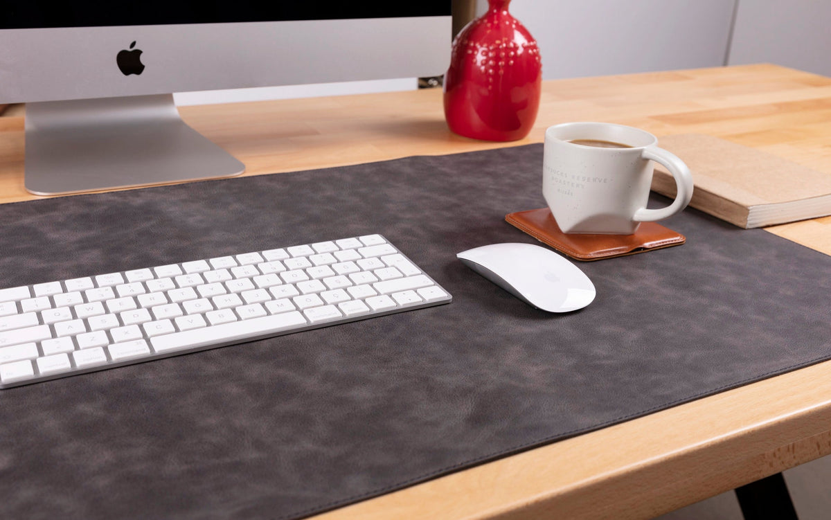 Desk setup with computer monitor, keyboard, mouse, and mug on a dark gray mat.
