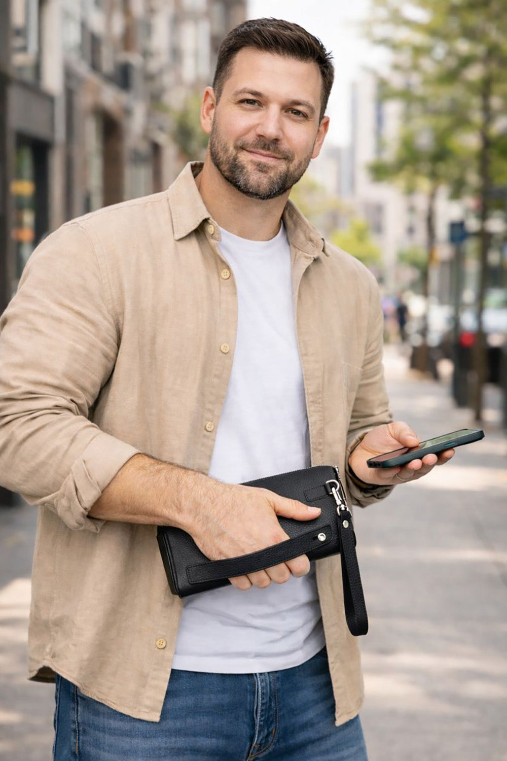 Man holding a phone and a black leather wallet on a city street.