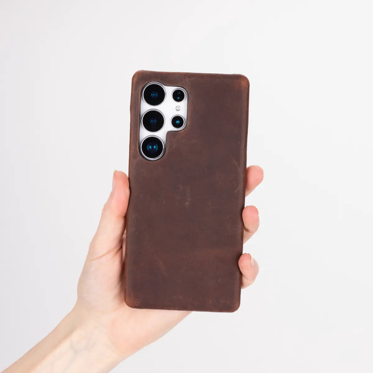 Hand holding a brown S25 phone case against a light gray background