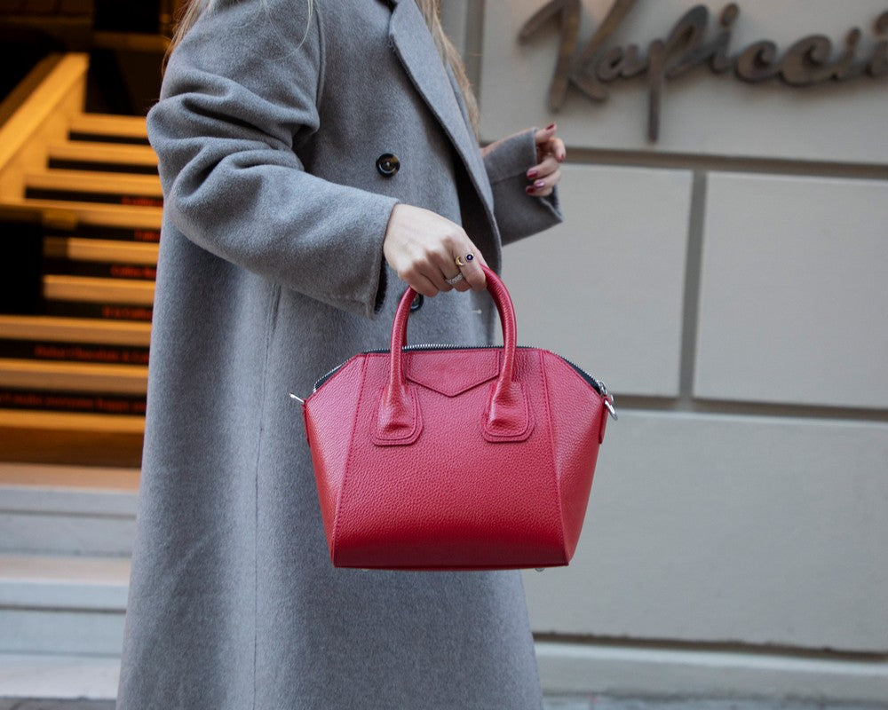 Person wearing a gray coat holding a red handbag in front of a building with 'Naples' sign.