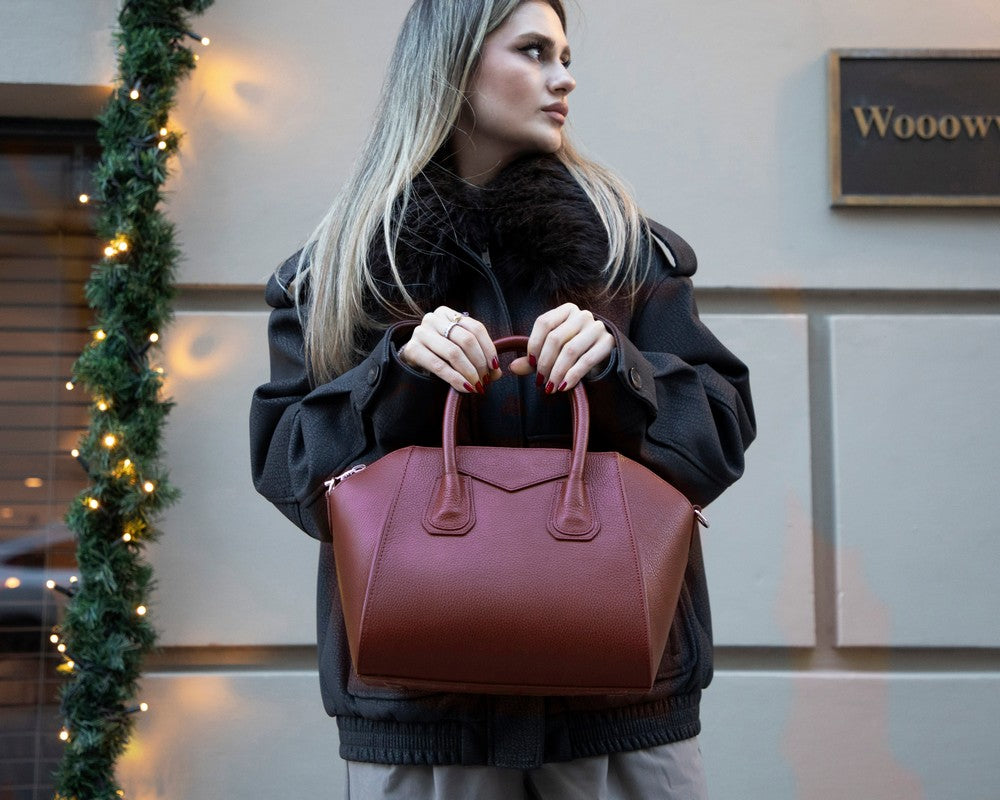 Woman holding a maroon handbag in an urban setting with decorative lights.