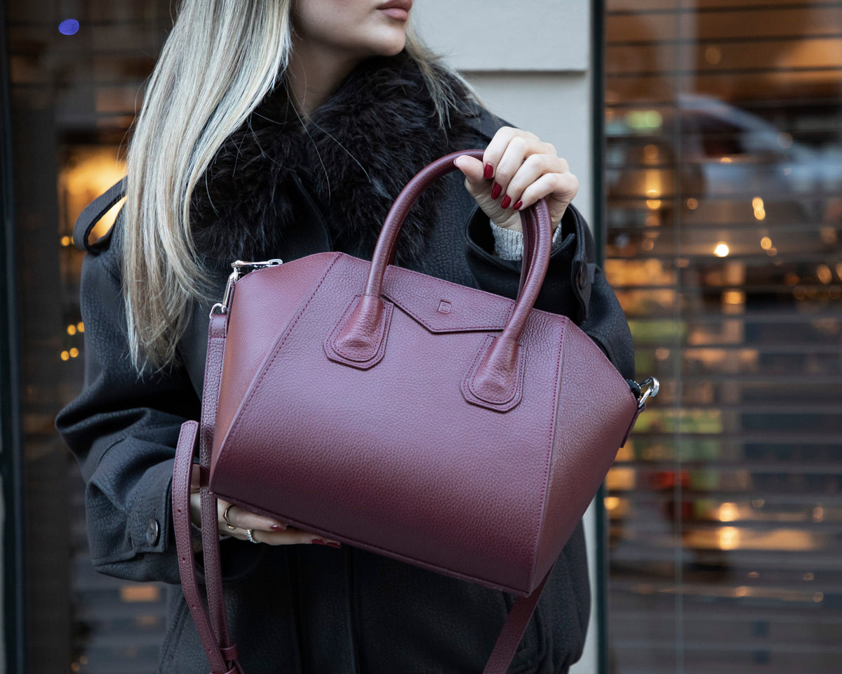 Person holding a maroon handbag with a blurred background