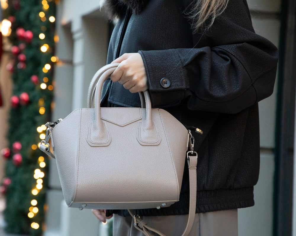 Person holding a beige handbag with festive lights in the background