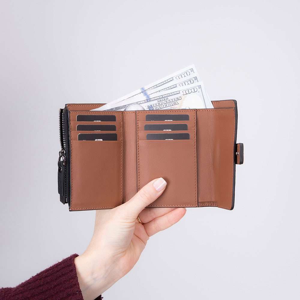 Brown wallet with money held open by a hand against a light gray background