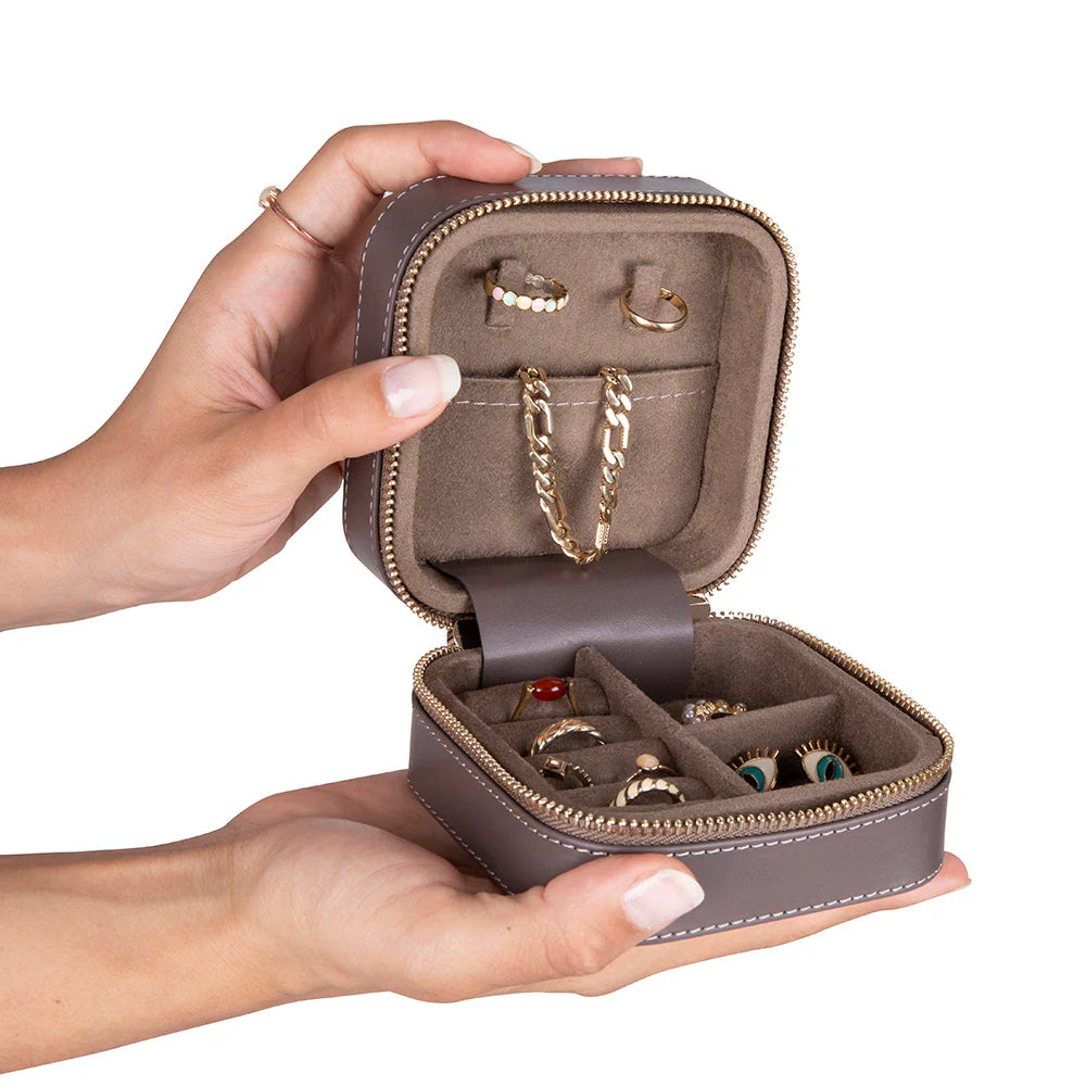 Hand holding a small brown jewelry case with gold jewelry inside on a white background