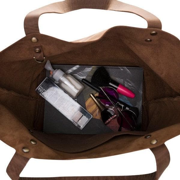 Brown leather bag with a clear compartment showing makeup items on a white background